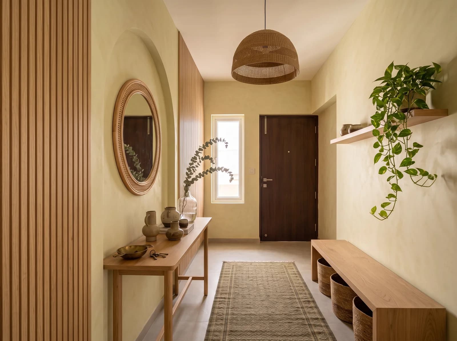Japandi foyer with a plain plaster arch, a round rattan mirror, an oak console with eucalyptus, a slatted oak wall and a bench with jute baskets
