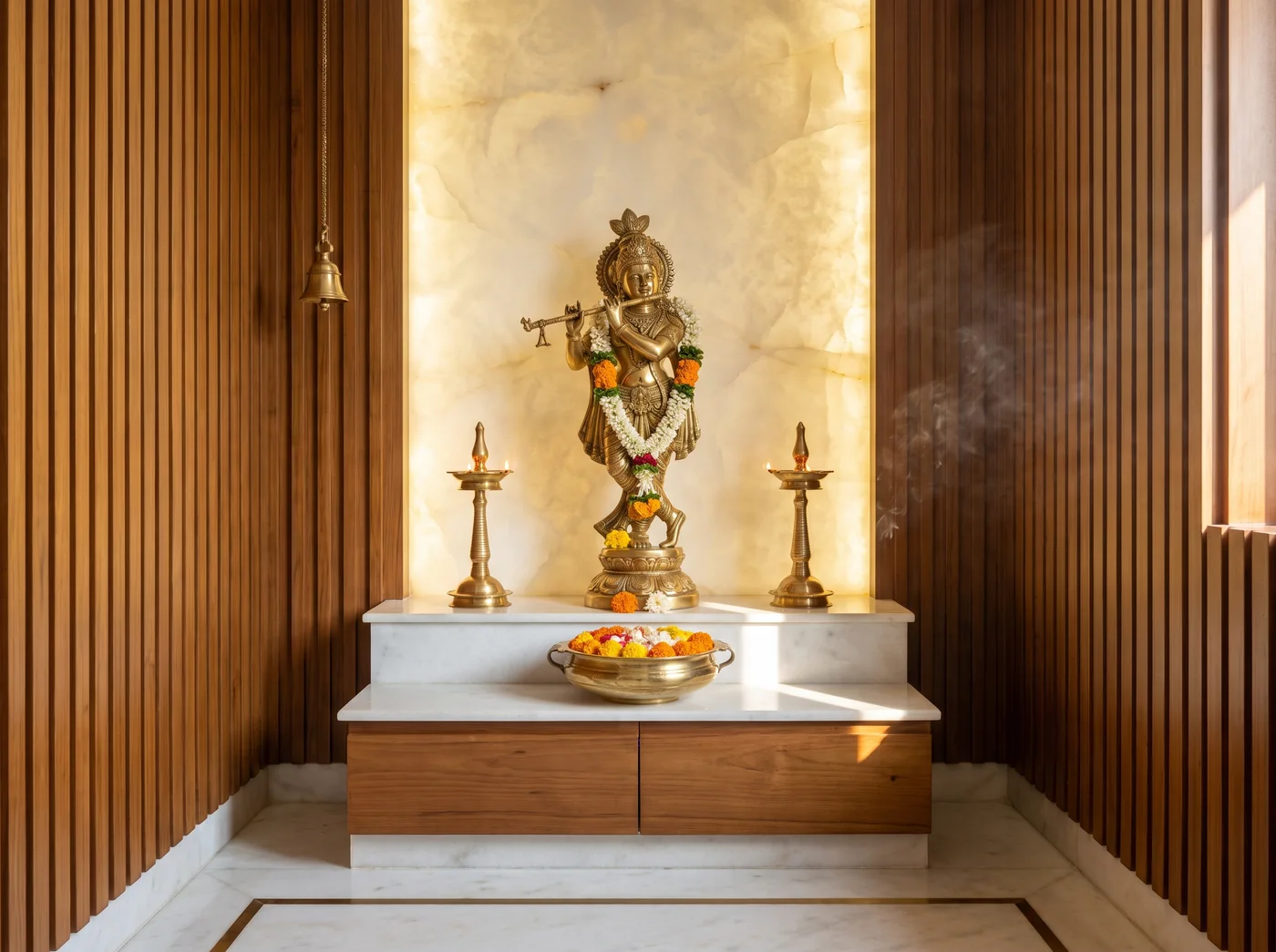 Pooja room with a standing brass idol on a marble altar, a backlit onyx wall, diyas and fresh flowers