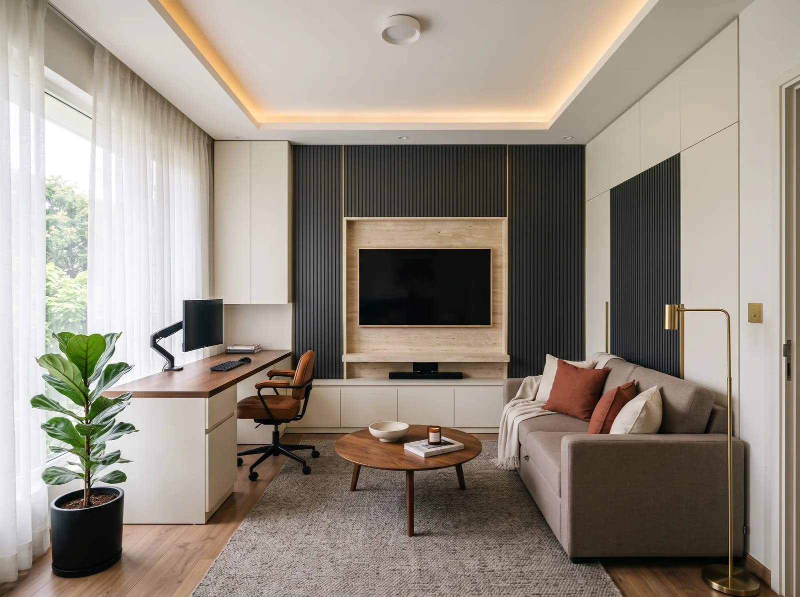 Modern luxury multipurpose room in a Bengaluru apartment by day: a media wall with a television set into a honed travertine niche with a floating stone ledge, charcoal fluted matt PU panels either side and warm-white PU cabinets beneath, a built-in walnut-topped desk under the window with overhead cabinets and a leather chair, a taupe sofa-cum-bed with rust cushions, a round walnut coffee table on a grey wool rug over engineered oak flooring, a brass floor lamp and a fiddle-leaf fig