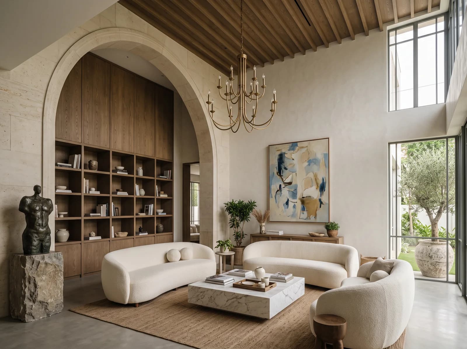 Double-height living room with a limestone arch onto a fumed oak library wall, a ribbed oak ceiling, a brass chandelier, curved ivory bouclé sofas and a bronze sculpture